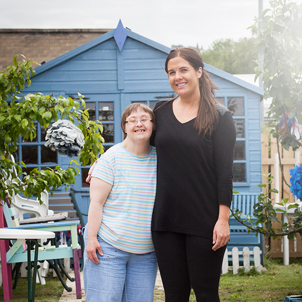 Female adult care worker with service user in a garden both smiling at the camera