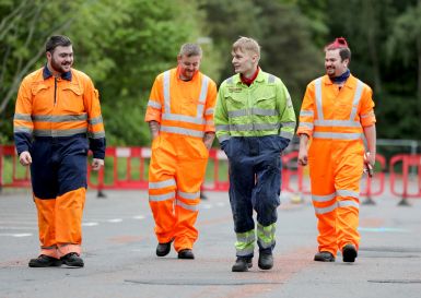 Four men in hi-viz outfits walking down a road